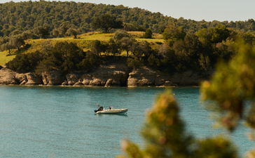 Turquoise waters and golden hillside at Amanzoe's beach club, with a moored boat visible offshore.