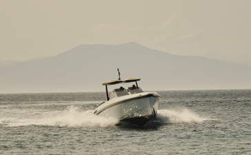 Wally One powerboat moored in calm waters off Amanzoe, with distant mountains visible under hazy skies.