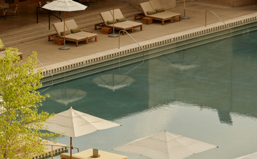 Amangiri's indoor plunge pool with pendant lighting, wooden loungers and cream umbrellas reflected in still water.