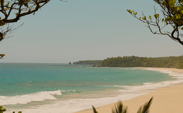 Plage de sable blanc et eaux turquoise vues entre la végétation tropicale à Amanera, resort en République dominicaine.