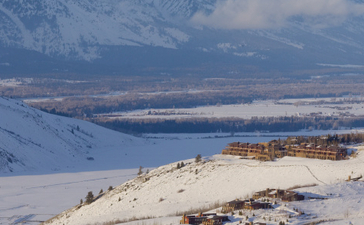 Snow-covered landscape surrounding Amangani in winter, with distant mountain peaks and valley below.