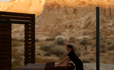 Therapist administering massage treatment at Amangiri wellness spa, with red rock cliffs visible beyond the pavilion.