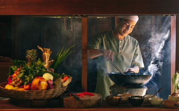 Chef preparing a meal in the open kitchen at Amansara's dining venue, with fresh ingredients displayed nearby.