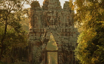 Stone temple tower framed by tree-lined avenue at Amansara, Cambodia, with statue in foreground.