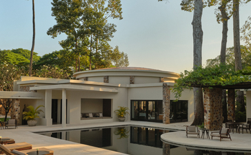 Amansara's main pool pavilion with wooden loungers, surrounded by tropical trees and manicured gardens.