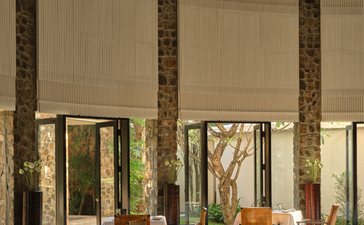 Dining room at Amansara with tall wooden columns, set table, and garden views through large windows.