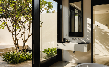 Amansara suite bathroom with vessel sink, large mirror, and open door leading to garden courtyard with potted plant.