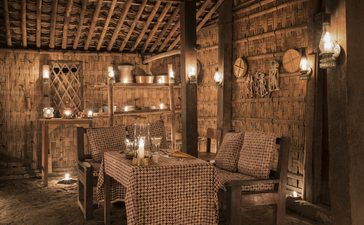 Candlelit dining room at Amanjiwo with woven wood walls and a table set for dinner in Java, Indonesia.
