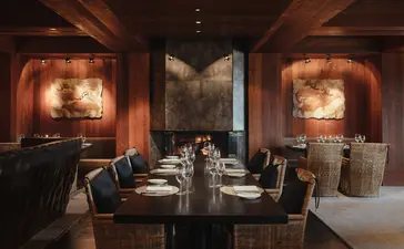 Amangani's dining venue with warm-lit alcoves, dark wood accents, and a long table set for service.