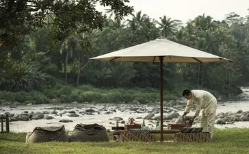 Amanjiwo staff member seated by the Progo River in Magelang, Central Java, beneath a white parasol.