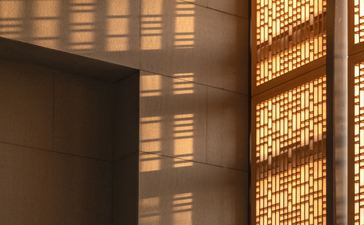 Warm light filters through a timber screen at Amanyangyun, casting geometric shadows on a dark wall.