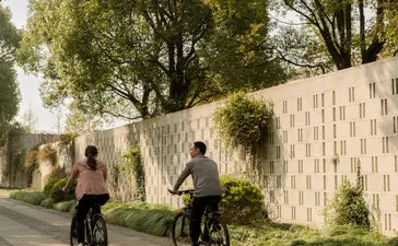 Cyclists riding along a tree-lined path at Amanyangyun, China, past contemporary architecture with climbing vines.