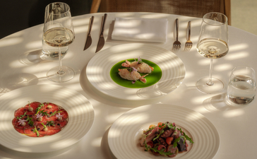 Dining table at Amanyangyun with three plated dishes and place settings, dappled sunlight across white tablecloth.