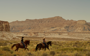Two riders on horseback traversing the desert landscape at Amangiri, with red rock formations in the distance.
