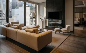 Sunlit living room at Aman New York with curved caramel sofa, floor-to-ceiling windows, and city views.
