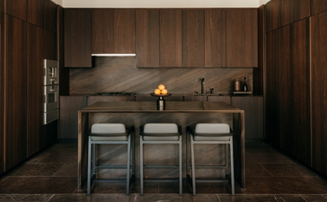 Cucina con boiserie in legno scuro e tre sgabelli al bancone presso Aman New York.