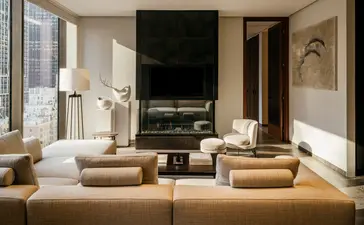 Serene lounge at Aman New York with neutral seating, fireplace, and floor-to-ceiling windows overlooking the city.
