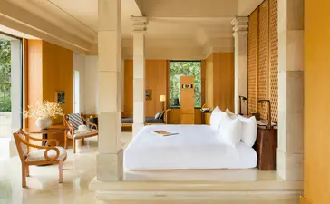 Suite bedroom at Amanjiwo with stone columns, white bed, and warm natural light from large windows.