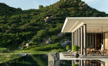 Beach club exterior at Amanoi, Vietnam, with a modern pavilion reflected in still water and forested hillside beyond.