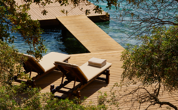 Wooden lounger on sandy beach at Amanruya, overlooking turquoise waters.