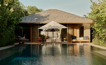 Amanyara pavilion with thatched roof reflected in still pool, surrounded by tropical vegetation.