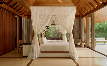 Amanyara pavilion with wooden beams framing a four-poster bed draped in cream fabric.