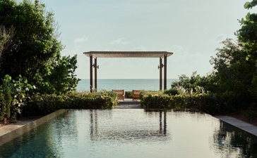 Amanyara pavilion reflected in still water, with tropical vegetation framing the scene.