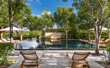 Duas espreguiçadeiras viradas para a piscina e jardins arborizado da villa de cinco quartos em Amanyara.