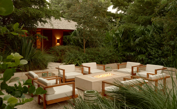 Four-bedroom villa outdoor seating area at Amanyara, Turks and Caicos, with wooden furniture beneath tropical trees.
