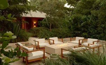 Sala de estar ao ar livre com sofás em tons neutros e almofadas, iluminada por lanternas, rodeada por vegetação tropical em Amanyara.