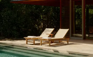Pavilhão da piscina em Amanyara, resort em Turks e Caicos, com espreguiçadeiras de madeira junto à água.