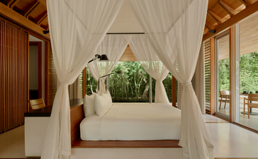 アマンヤラのプール・パビリオンにあるベッド、白いドレープと木製の柱に囲まれている