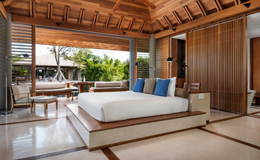 アマンヤラ リゾートの6ベッドルーム ビーチ サラ ヴィラの寝室。木製の天井と壁、青いクッション付きのベッド、開放的なテラスが見える。