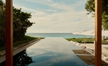 The Artists Villa at Amanyara overlooks turquoise waters and tropical coastline through open wooden shutters.