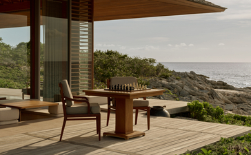 Wooden dining table and chairs on a terrace at Amanyara, overlooking the Turks and Caicos coastline.