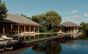 アマンヤラのターコス・カイコス島の3ベッドルーム・トランクイリティ・ヴィラ。池を挟んで建つ木造建築物と、青空の下の静かな水景。