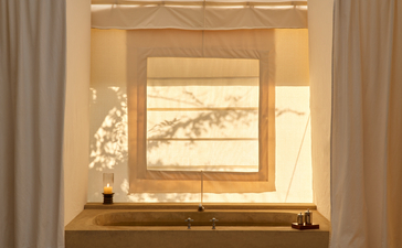 Bathtub set into wooden surround within tent bathroom at Aman-i-Khas, with framed artwork above and sheer curtains either side.
