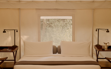 Tent bedroom at Aman-i-Khas with cream furnishings, symmetrical bedside tables and a central window overlooking Indian landscape.