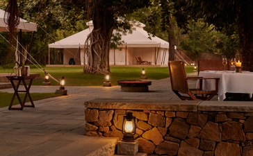 Tented pavilion at Aman-i-Khas illuminated at dusk, surrounded by trees and a stone firepit.