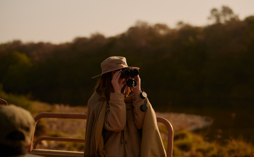 Safari guide at Aman-i-Khas observing wildlife through binoculars at dusk.