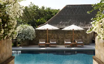 Resort swimming pool at Aman Villas at Nusa Dua, Indonesia, with thatched pavilion and loungers.