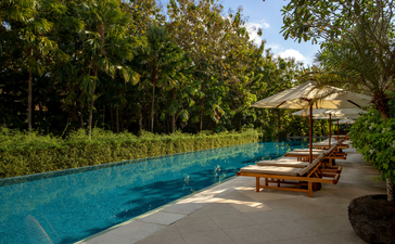 Resort swimming pool at Aman Villas at Nusa Dua, flanked by loungers and tropical trees.