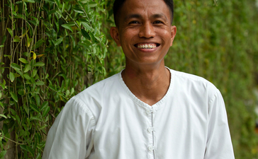 Private butler at Aman Villas at Nusa Dua, Indonesia, standing against vine-covered wall.