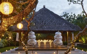 Candlelit pathway through manicured gardens at Aman Villas at Nusa Dua, leading to an illuminated pavilion at dusk.