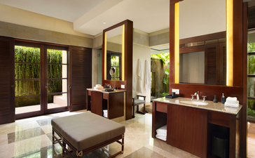 Principal bedroom with ensuite bathroom at Aman Villas at Nusa Dua, featuring dark wood furnishings and warm lighting.