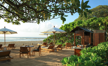 Beachfront terrace at Aman Villas at Nusa Dua with wooden loungers, tropical plants, and ocean views.