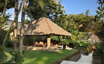Thatched-roof dining pavilion at Aman Villas at Nusa Dua, surrounded by tropical gardens and palm trees.