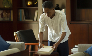 A woman sits reading in the resort library at Aman Villas at Nusa Dua, surrounded by warm wooden shelving and soft lighting.