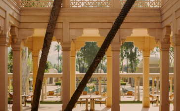 Amanbagh's main restaurant building exterior with geometric latticed windows and a large tree trunk passing through the sandy-coloured colonnade.