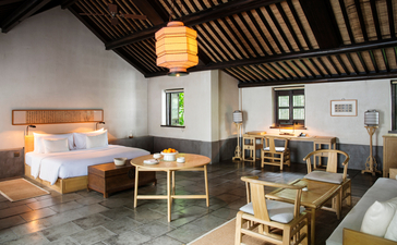 Amanfayun bedroom with wooden ceiling, two beds, seating area and dining space bathed in natural light.